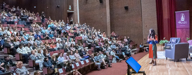 A female-presenting individual giving a lecture to a full auditorium